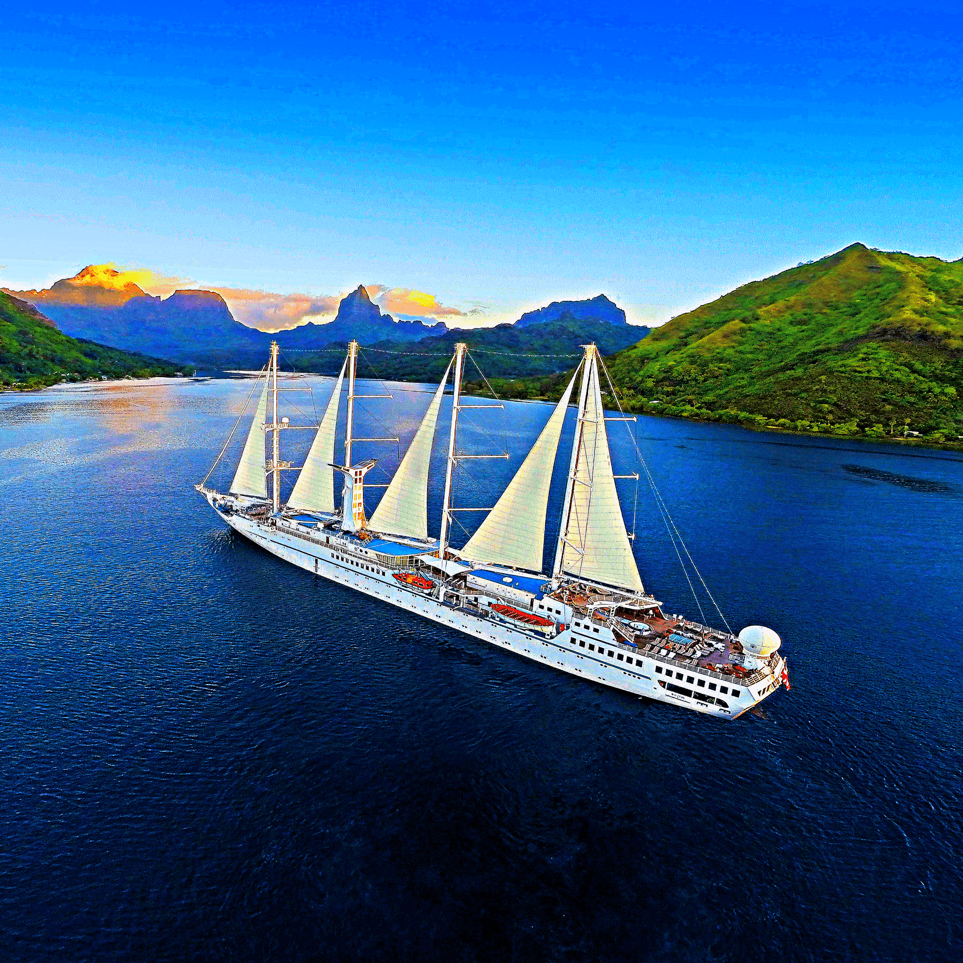 A large sailboat cruising through a scenic tropical landscape with lush green mountains and clear blue sky.